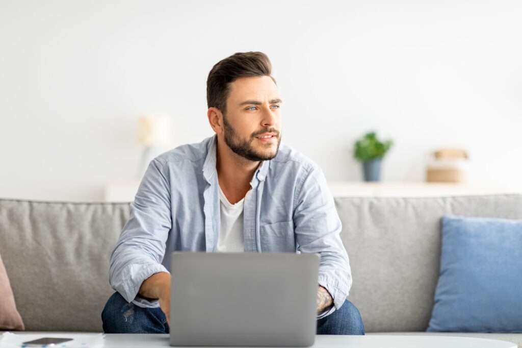 Un jeune freelance travaillant sur son ordinateur portable et regardant sur le côté, pensant à une entreprise prospère.